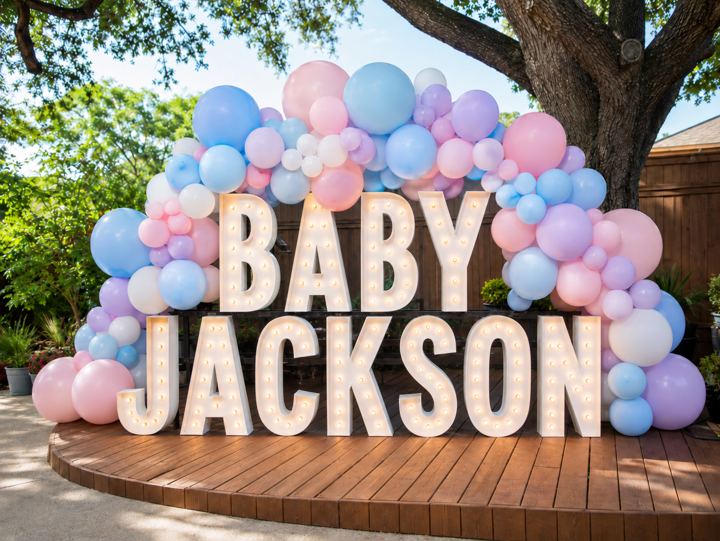 Vintage white bulb marquee letters spelling BABY JACKSON with pastel balloon garland