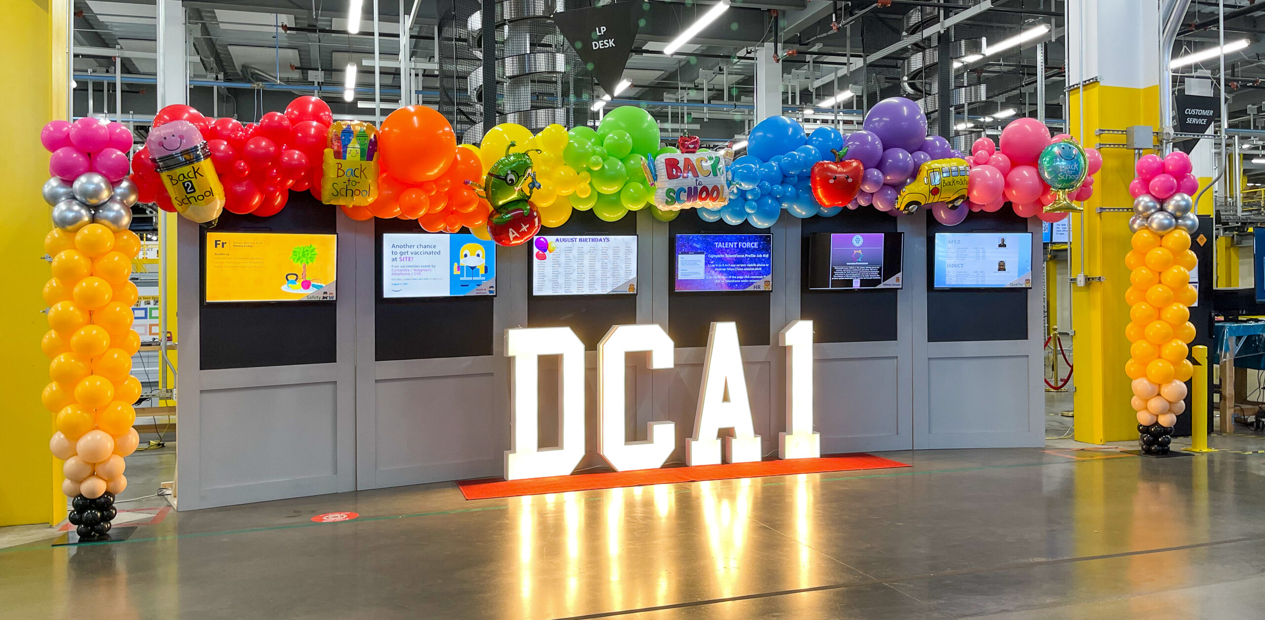 Rainbow organic balloon garland over the DCA1 marquee at an Amazon fulfillment center