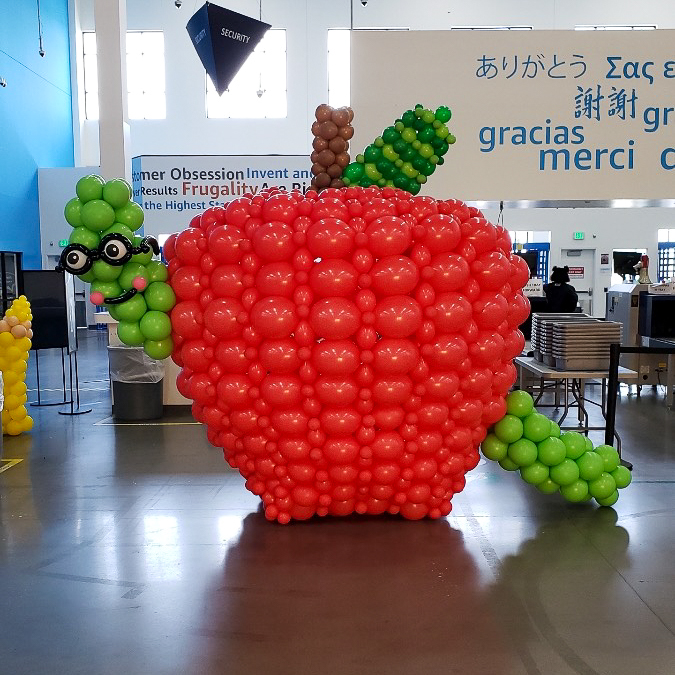 Giant apple and reading worm balloon sculpture at an Amazon back-to-school event